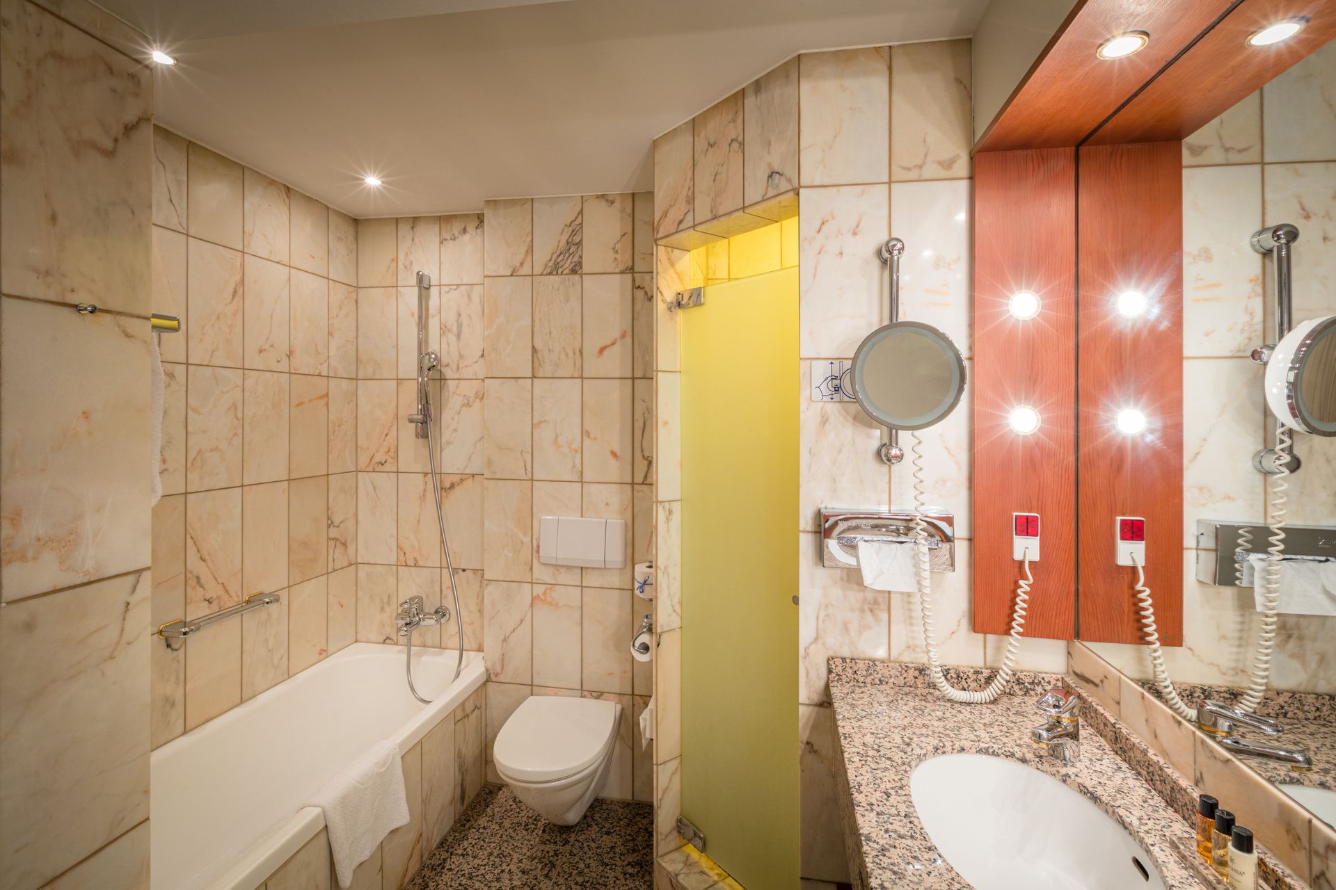 Badeværelse med marmorfliser på vægge, hvidt badekar, toilet og håndvask samt bruseniche.