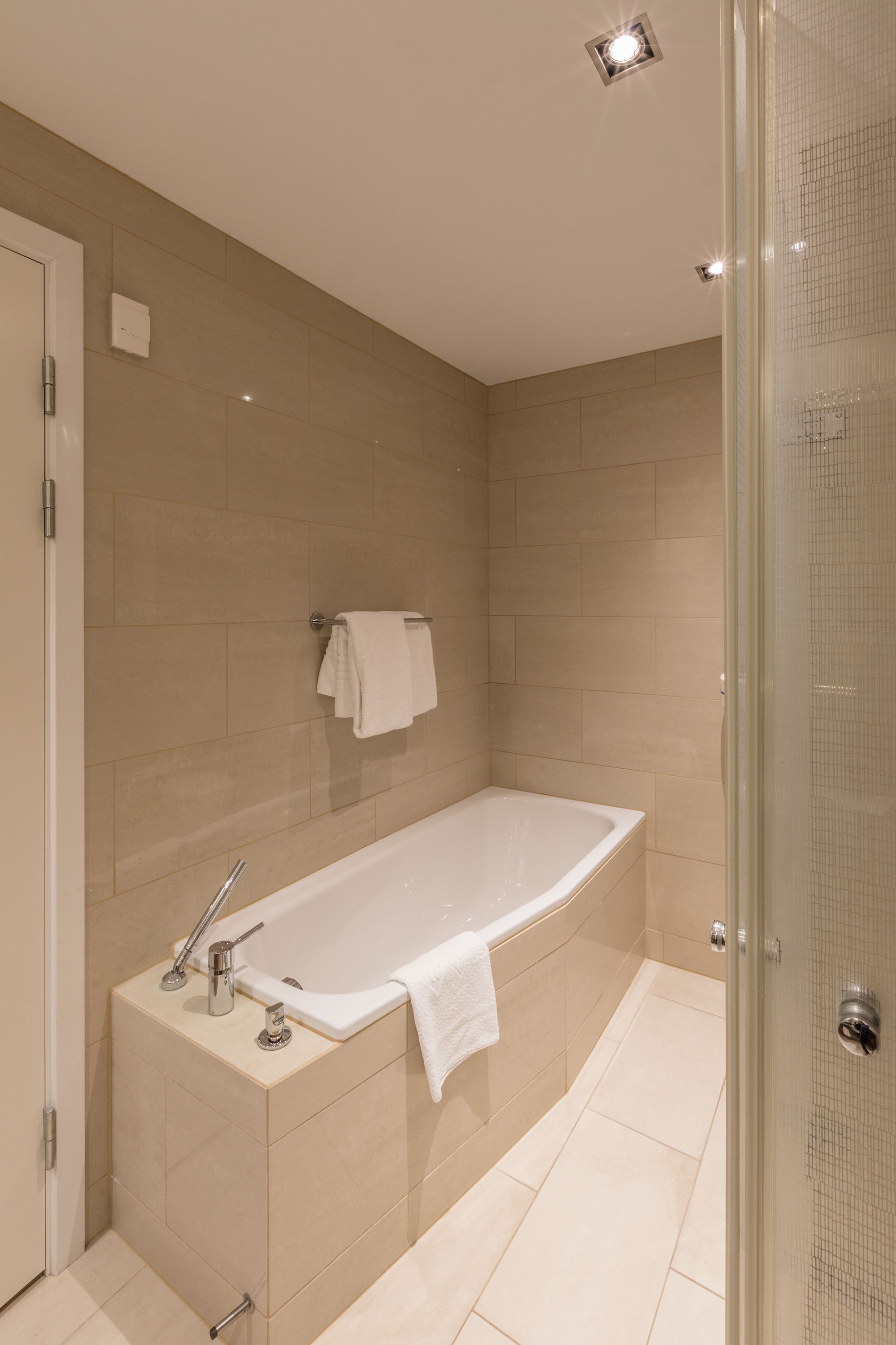 Moderne badeværelse med badekar, hvide håndklæder og beige fliser på væggene.