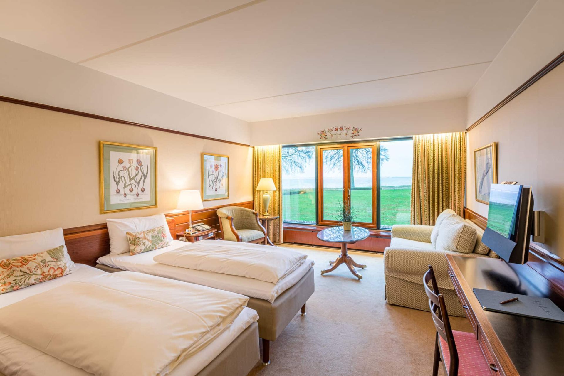 Et hotelværelse med to senge, en sofa, et skrivebord og et fjernsyn.