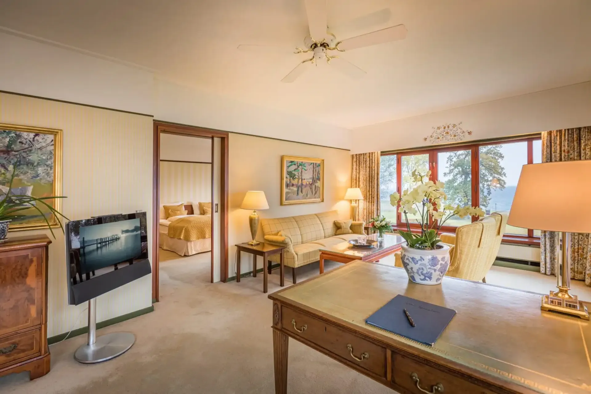 En stue med skrivebord, sofa, fjernsyn og loftsventilator.