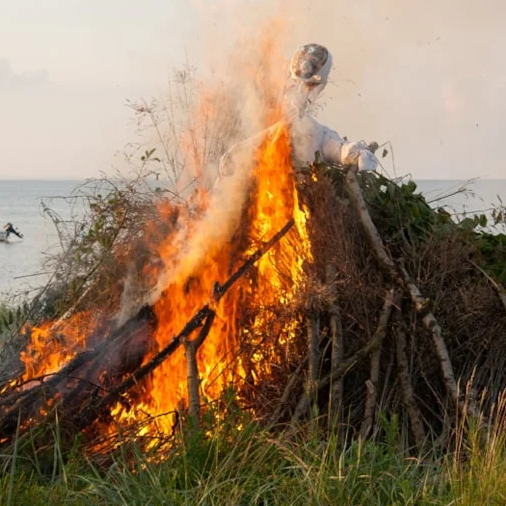 Et fugleskræmsel står foran et stort bål.