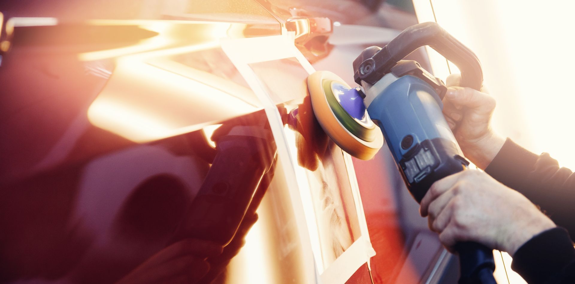 A mechanic sands the putty on a car body with a machine.