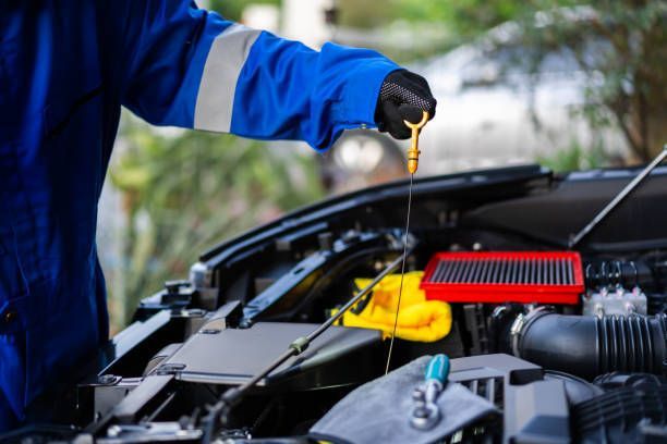 Mechanic checking car engine oil level with dipstick, wearing blue uniform and gloves.