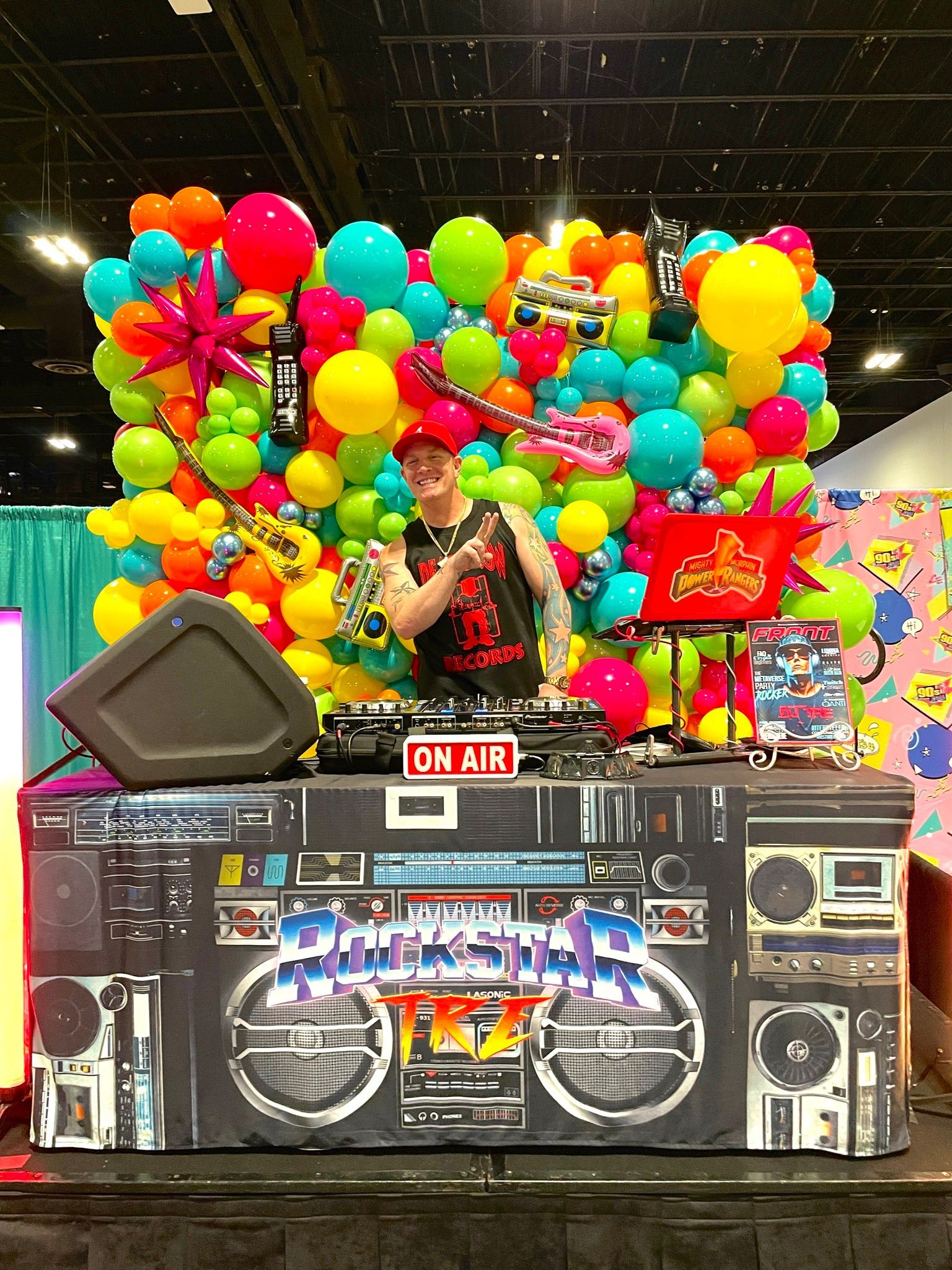 A dj is standing in front of a wall of colorful balloons.
