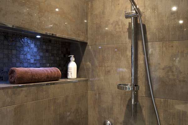 A shower with a towel and a bottle of lotion on a shelf.