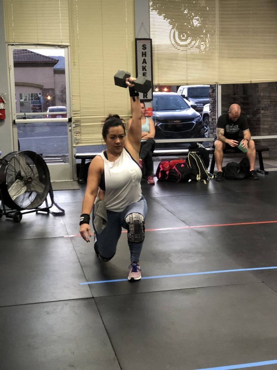 A woman is lifting a dumbbell over her head in a gym.