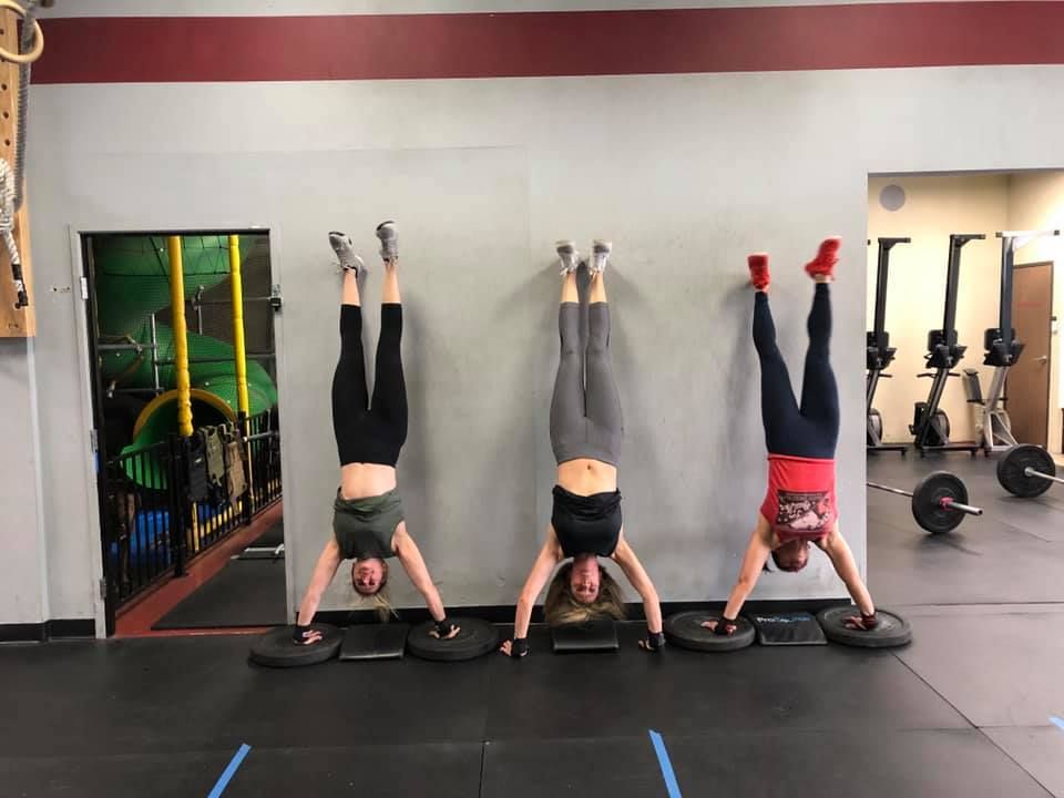 Three women are doing handstands against a wall in a gym.