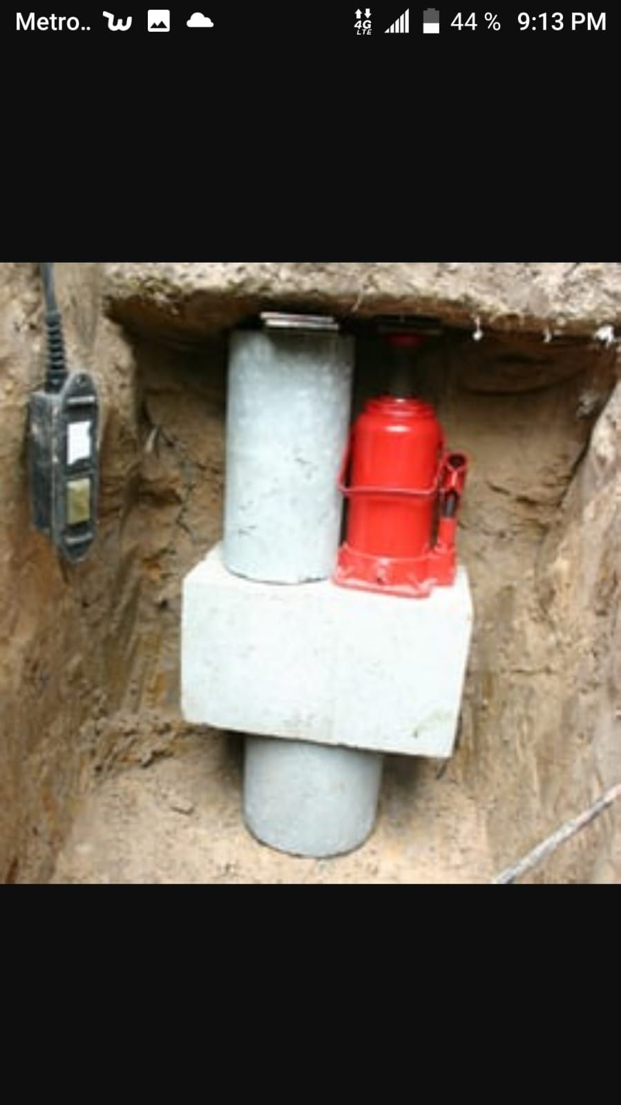 A red bottle is sitting on top of a concrete block in a hole.