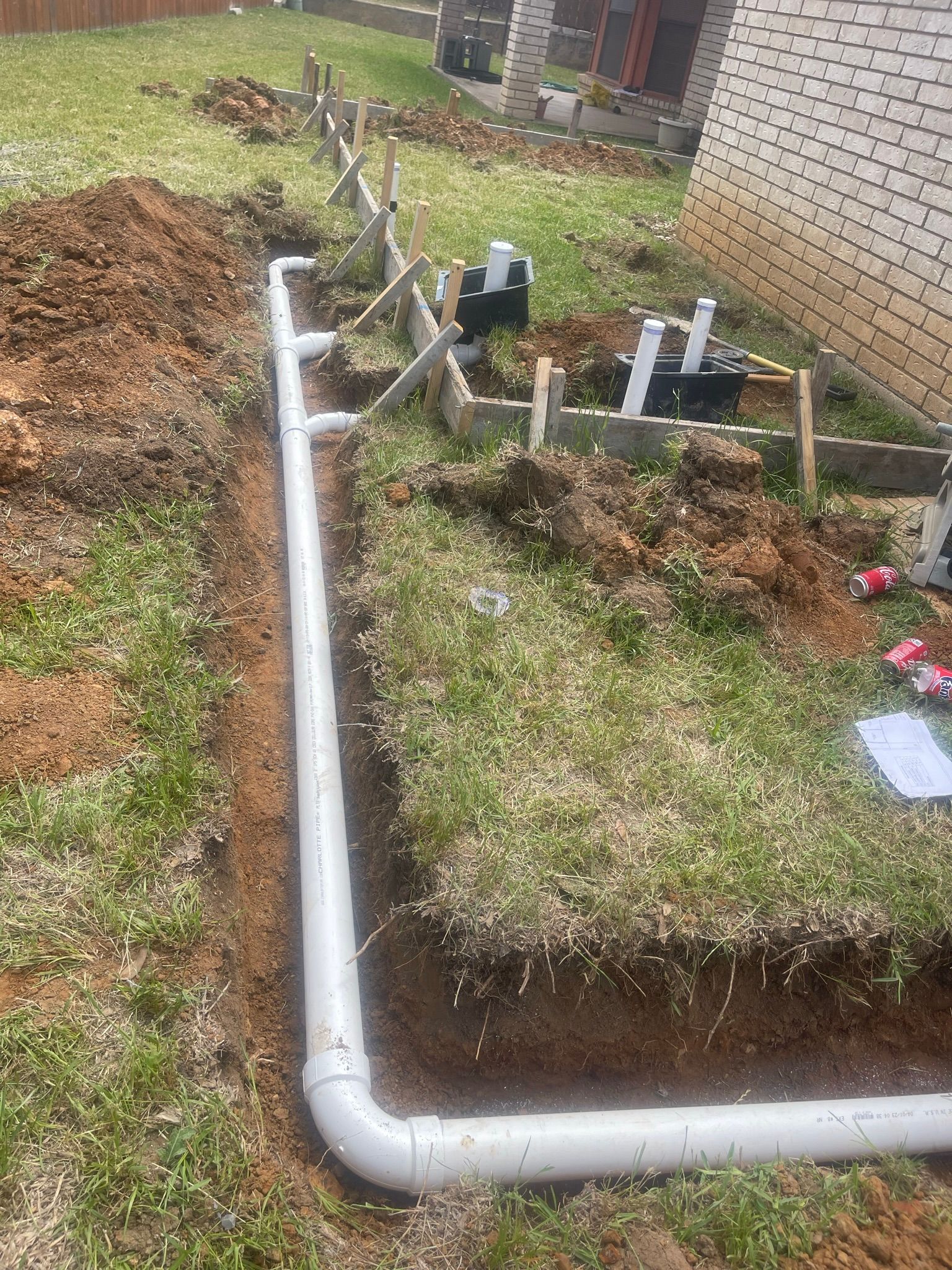 A white pipe is being installed in the dirt in a yard.