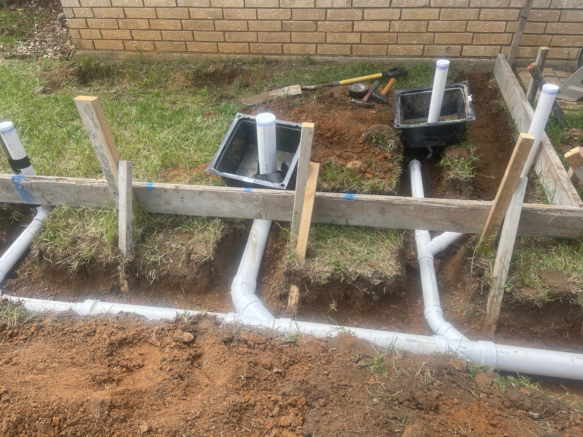 A bunch of pipes are being installed in the dirt in front of a brick building.