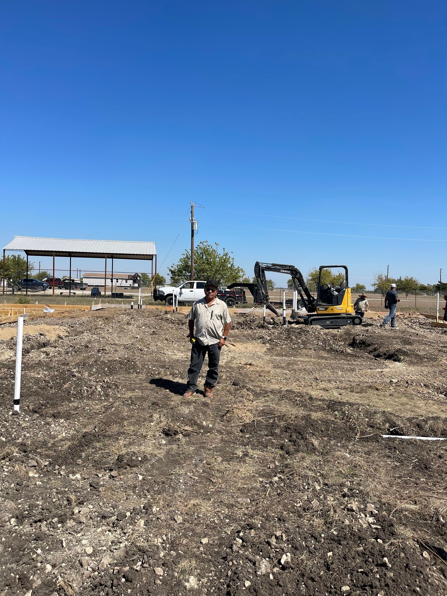 A man is standing in a dirt field with a bulldozer in the background.