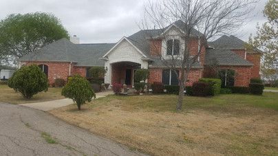 A large brick house with a gray roof is sitting on top of a lush green lawn.