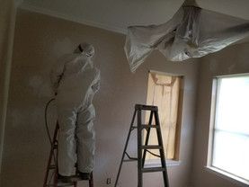 A man in a protective suit is standing on a ladder in a room.