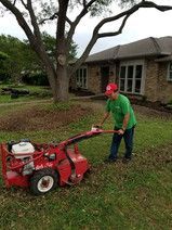 A man is using a lawn mower to remove leaves from a lawn.