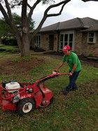 A man is using a lawn mower to cut the grass in front of a house.