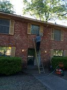 A man is standing on a ladder on the side of a brick building.