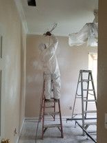 A man in a protective suit is standing on a ladder in a room.