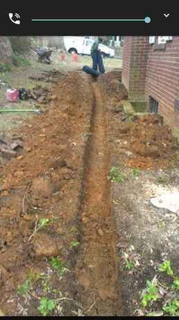 A man is digging a trench in the dirt in front of a house.