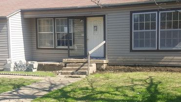 A small house with a porch and stairs in front of it.