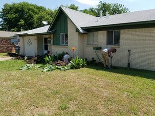 A group of people are working on a lawn in front of a house.