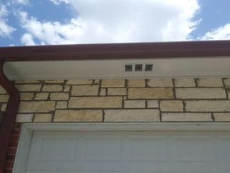 A brick wall with a white garage door and a gutter on it.