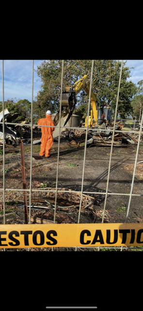 A man in an orange suit is standing in front of a yellow caution tape.