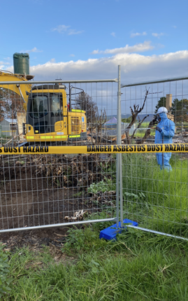 A man in a protective suit is standing in front of a fence.