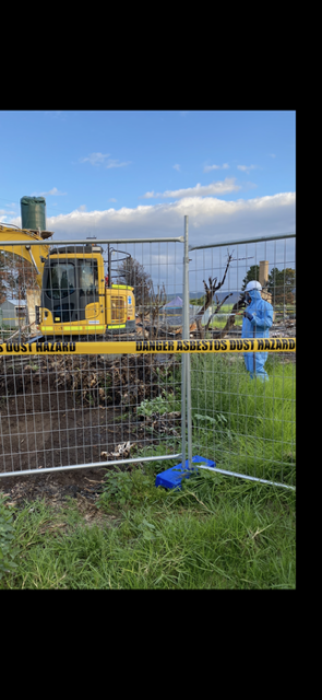 A yellow bulldozer is behind a fence in a field.