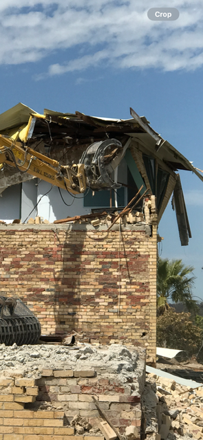 A brick building is being demolished by a crane.