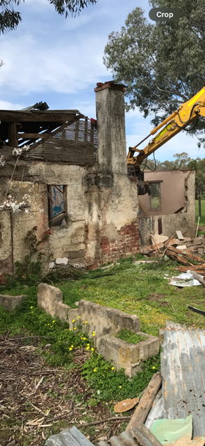 A yellow excavator is demolishing a brick building.
