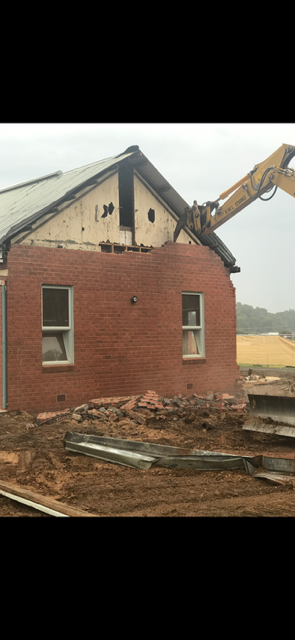 A brick house is being demolished by a bulldozer.