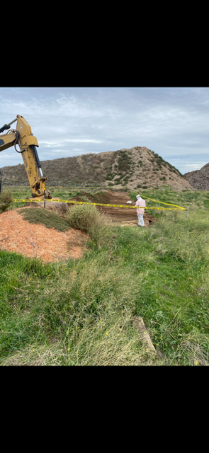 A bulldozer is digging a hole in the middle of a grassy field.