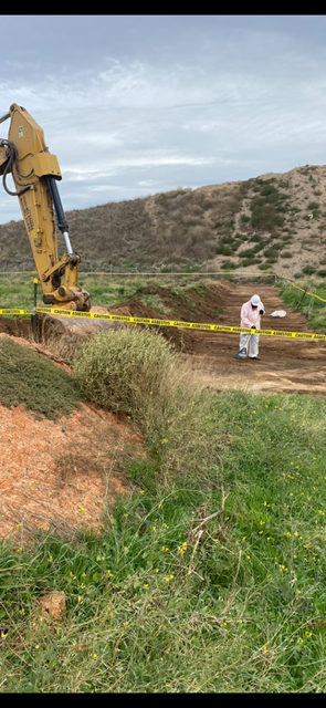 A man in a white suit is standing next to a bulldozer in a field.