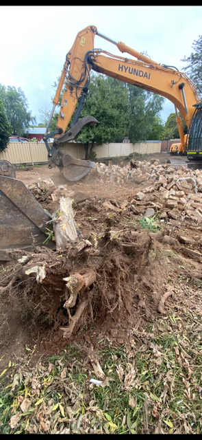 A large excavator is moving a tree stump out of the ground.