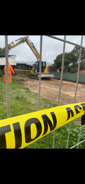 A yellow caution tape is hanging on a fence in front of a construction site.