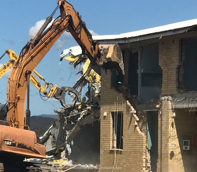 A cat excavator is demolishing a brick building