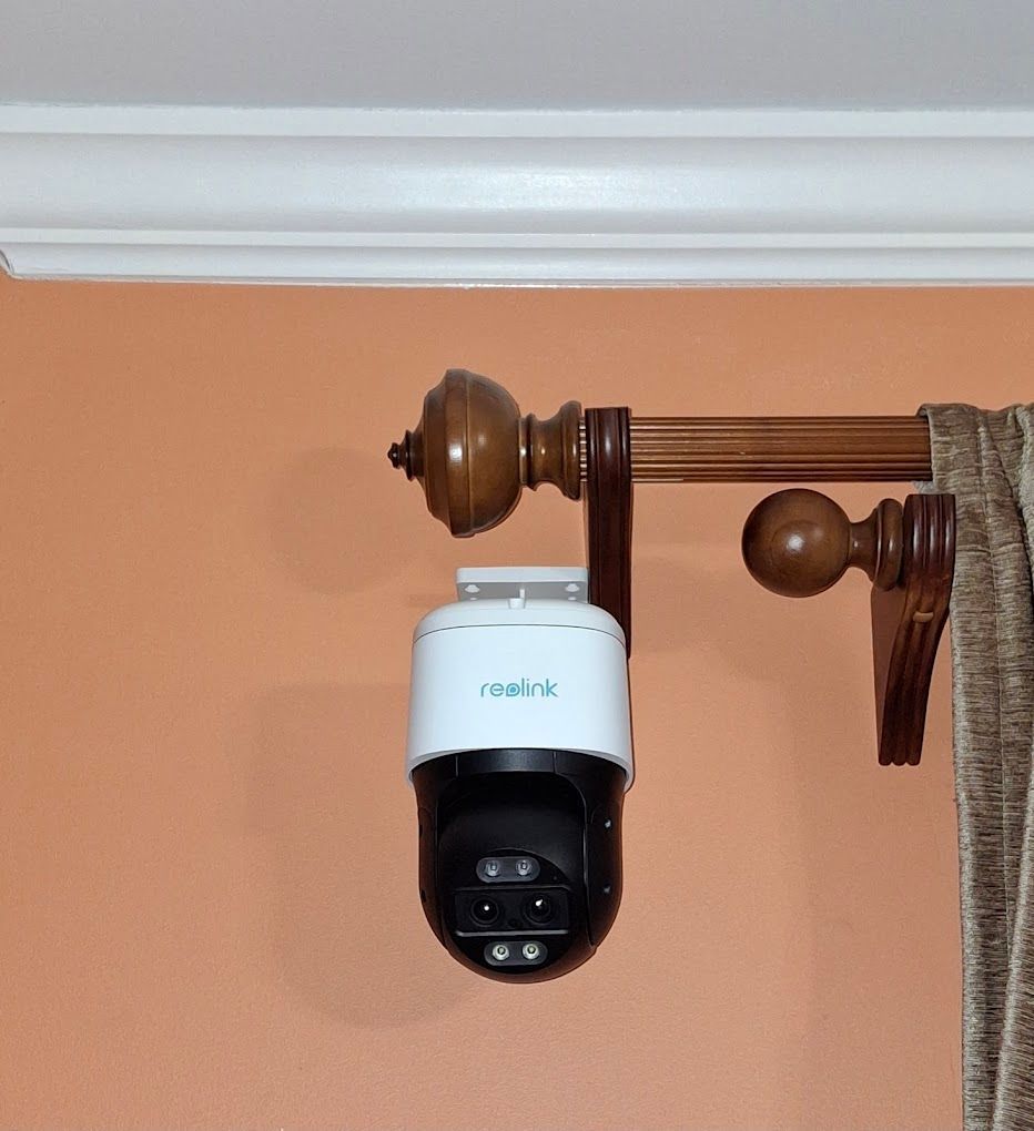 A security camera is hanging from the ceiling next to a curtain rod.