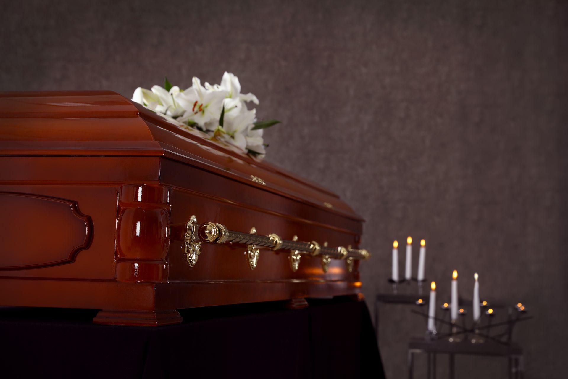 Wooden coffin with white flowers and lit candles in a dim funeral setting