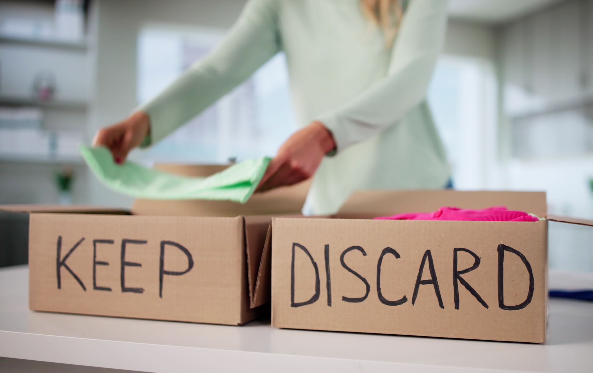 Close-up of a woman sorting clothes into “Keep” and “Discard” boxes.