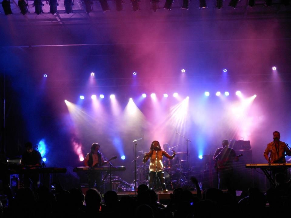 Band performing onstage under purple and blue lights with smoke and silhouetted musicians