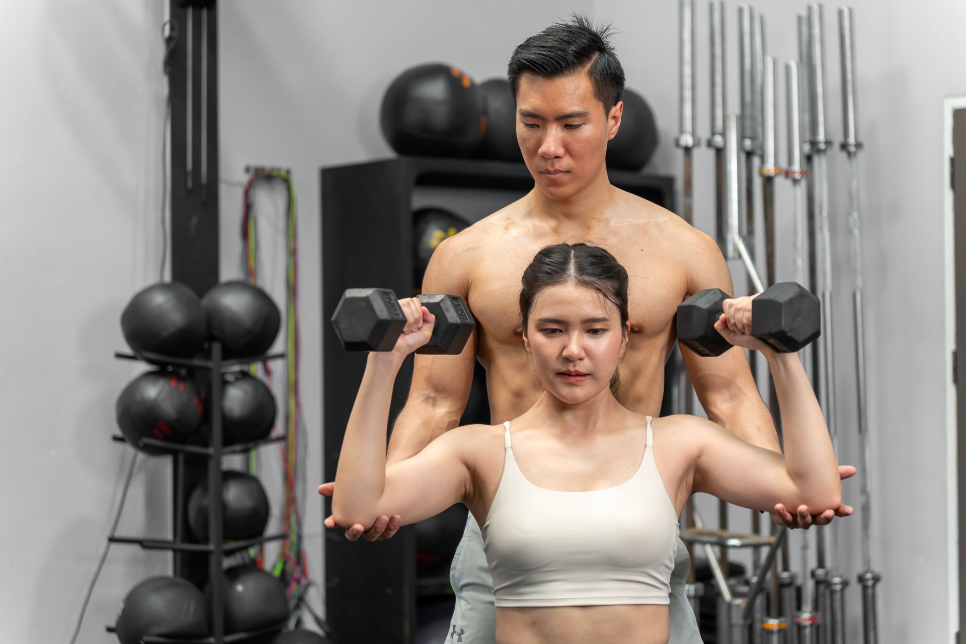 Woman lifting dumbbells with guidance from a trainer in a gym setting.