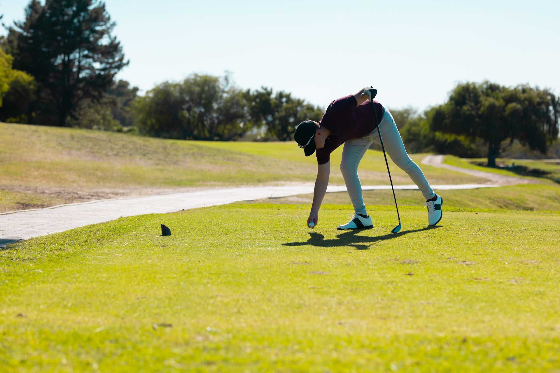 A golfer tees up a ball on a bright green golf course under a sunny sky.