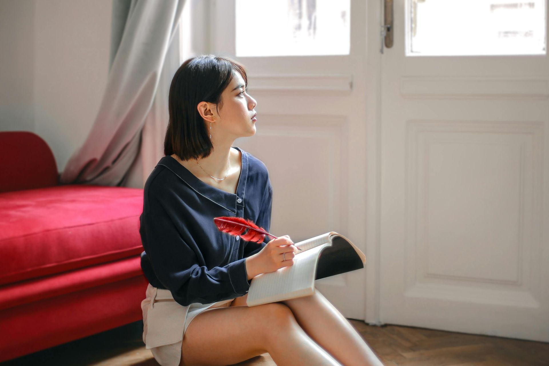 A woman is sitting on the floor holding a book and a pen.