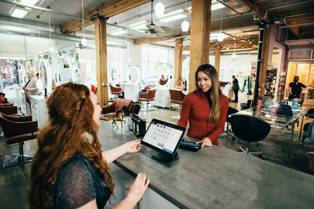 Two women discussing at a table in an open office, with a laptop in the foreground