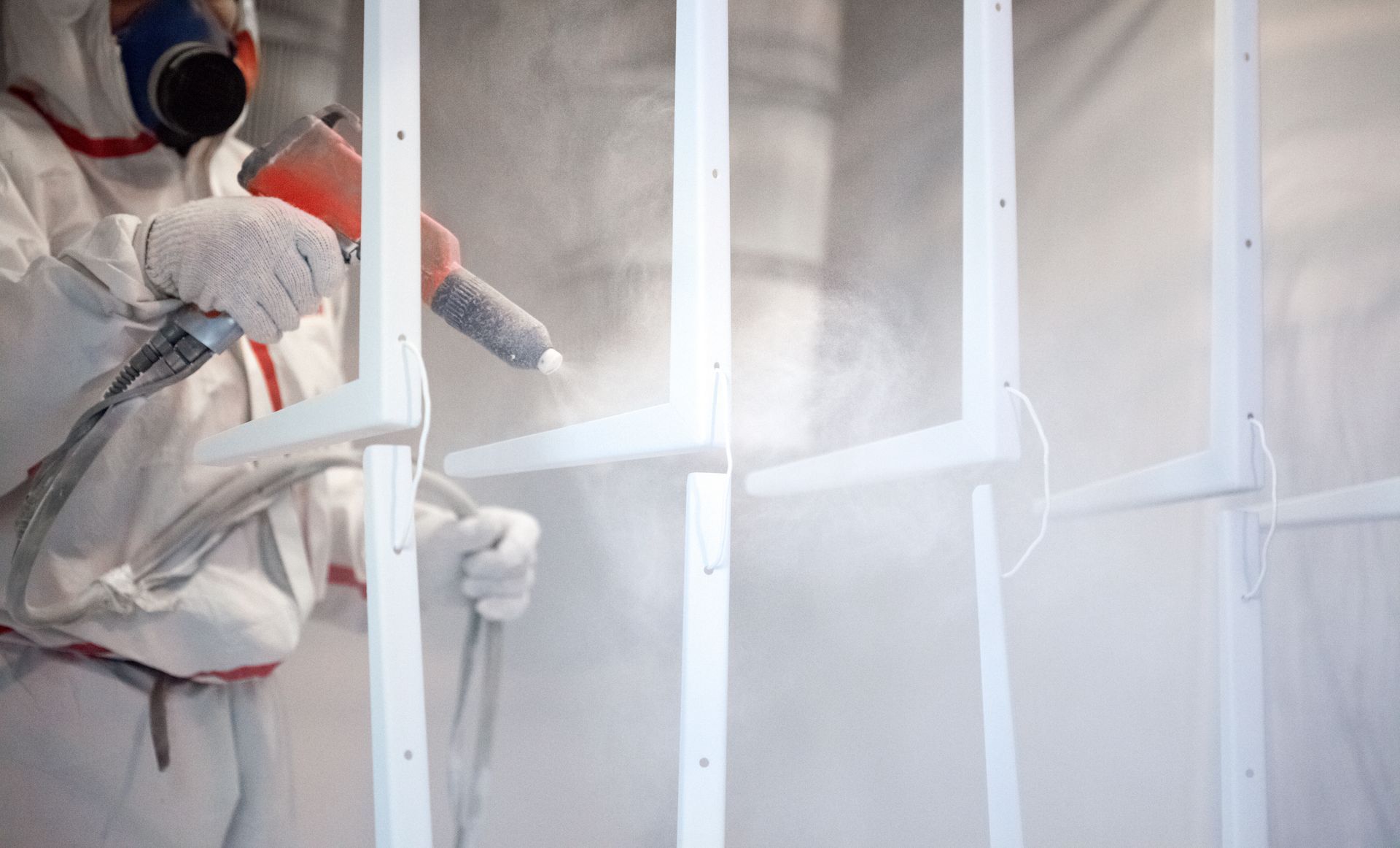 Person in protective suit powder coating white metal frames.