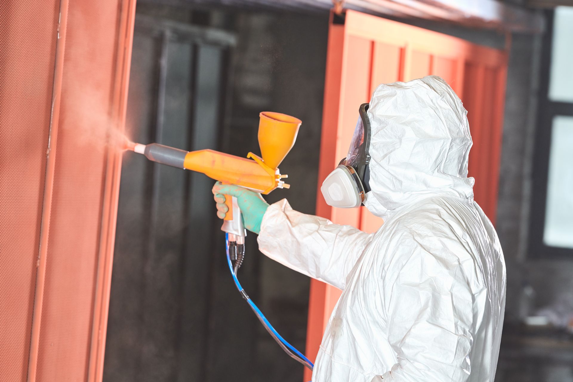 A man applying powder coating to what seems to be a metal garage door, using a protective suit. A man applying powder coating to what seems to be a metal garage door, using a protective suit.