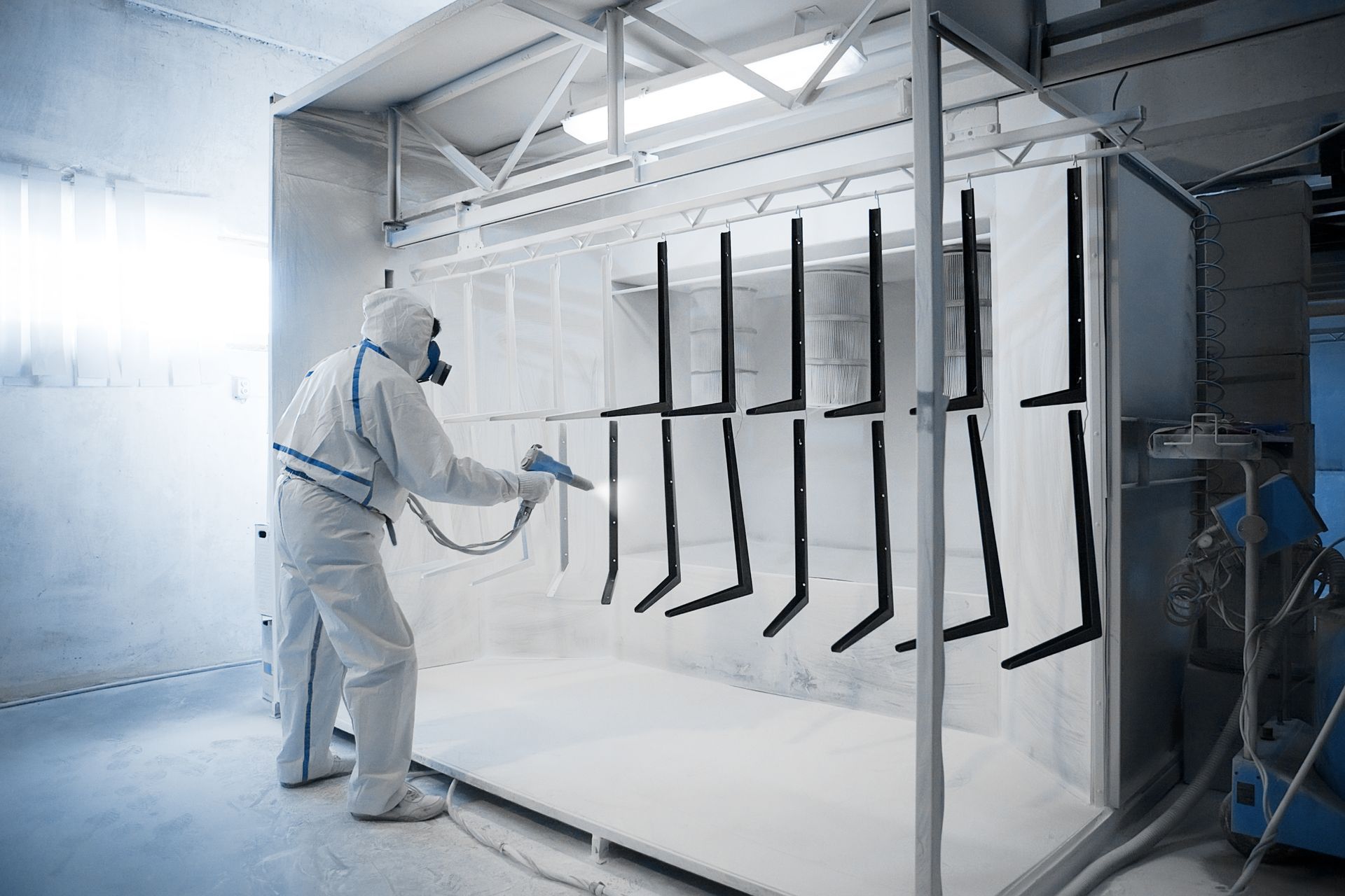 A Powder coating professional working with a protective suit and gear, painting metal sheets white. A Powder coating professional working with a protective suit and gear, painting metal sheets white.
