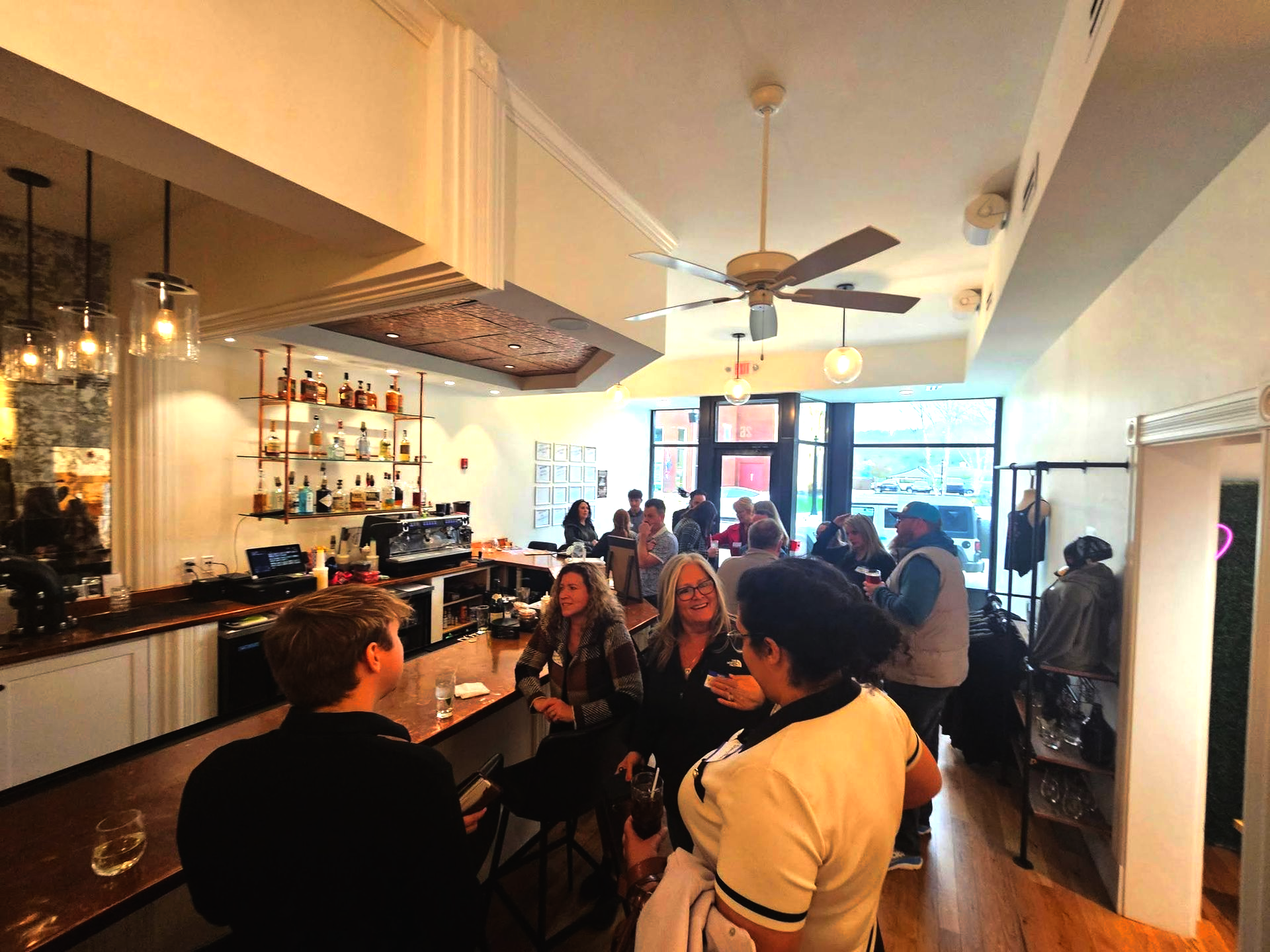People socializing in a bar; some at the counter, others standing. Lit bar area with drinks and bottles.