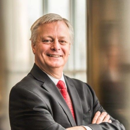 Alan L. Lindeman. Man in suit smiles, arms crossed. Gray hair, red tie, professional setting.