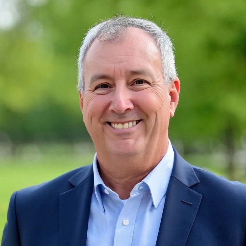 Dave Moravec. Smiling older man in a blue suit and light blue shirt; outdoors in a park-like setting.